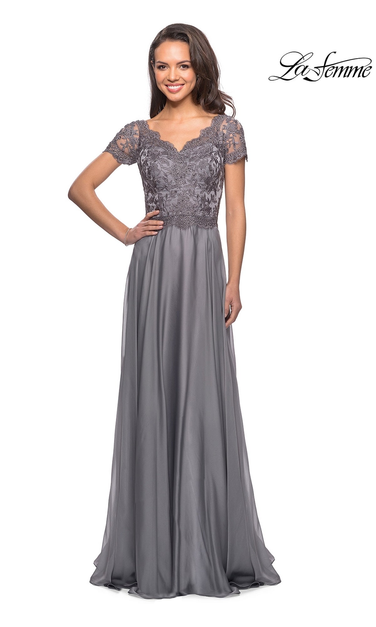 Woman wears Long Formal Dress: La Femme 27098—modest style with chiffon A-line skirt, lace embroidered bodice; smiling, hands on hips. “La Femme” logo top right.
